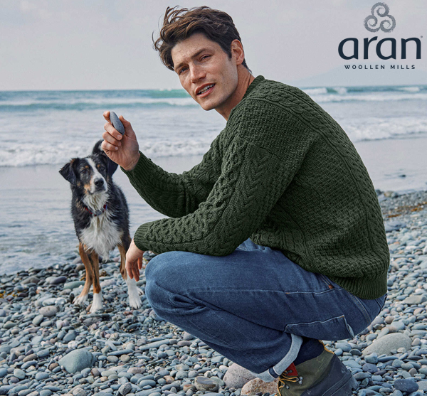 Mann im Aranpulli am Strand mit Hund
