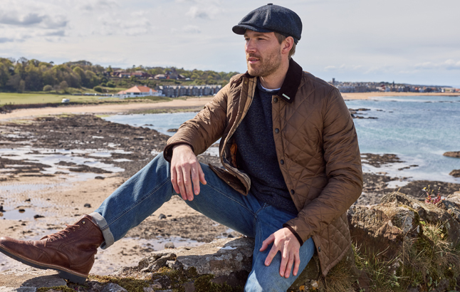 Mann in Steppjacke sitzt am Strand