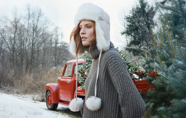Frau mit Lammfellmütze vor verschneitem Oldtimer