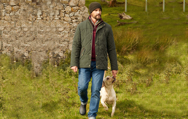 Mann in Steppjacke von Barbour mit Hund vor Steinmauer