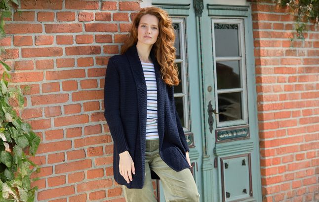 Frau in Strickjacke in navy lehnt an Hauswand