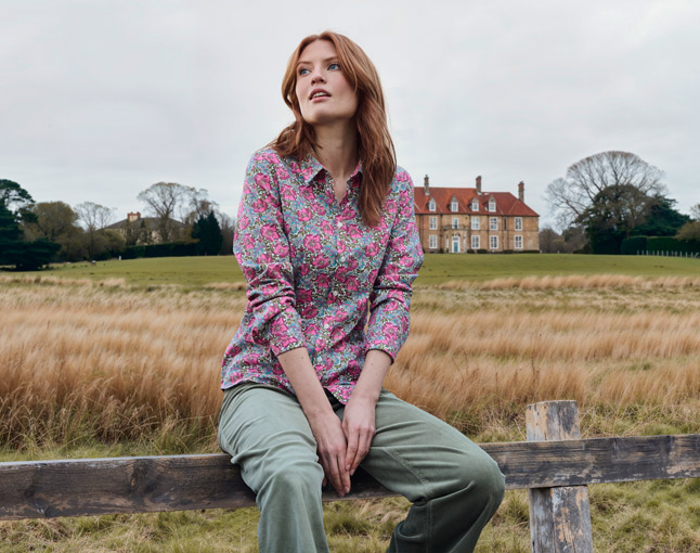 Frau sitzt auf Gatter vor großer Wiese