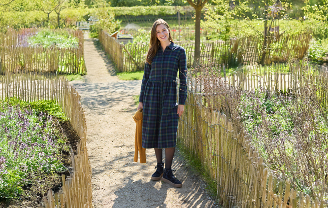 Frau im Flanellkleid vor Gartenzaun