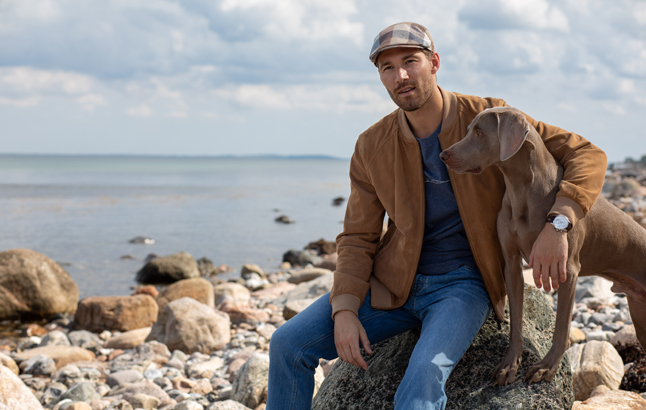 Mann sitzt mit Hund am Strand